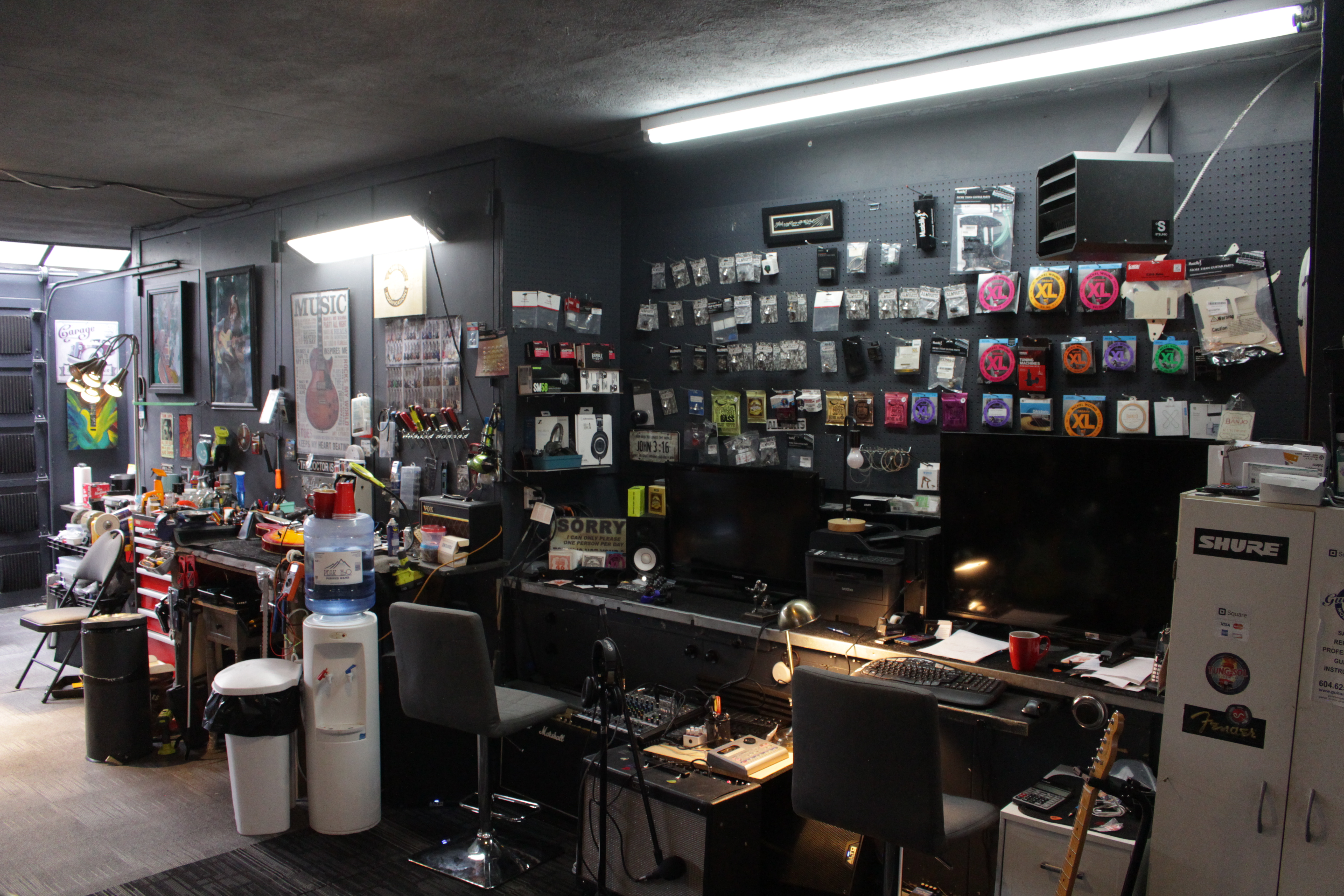 Professional guitar repair shop showing parts, accessories, and equipment wall storage